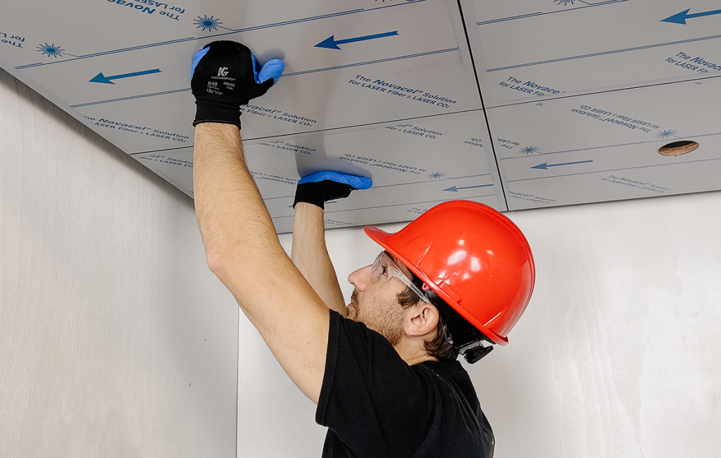 An installer wearing a red hard hat installing a steel ceiling panel during an elevator interior remodel