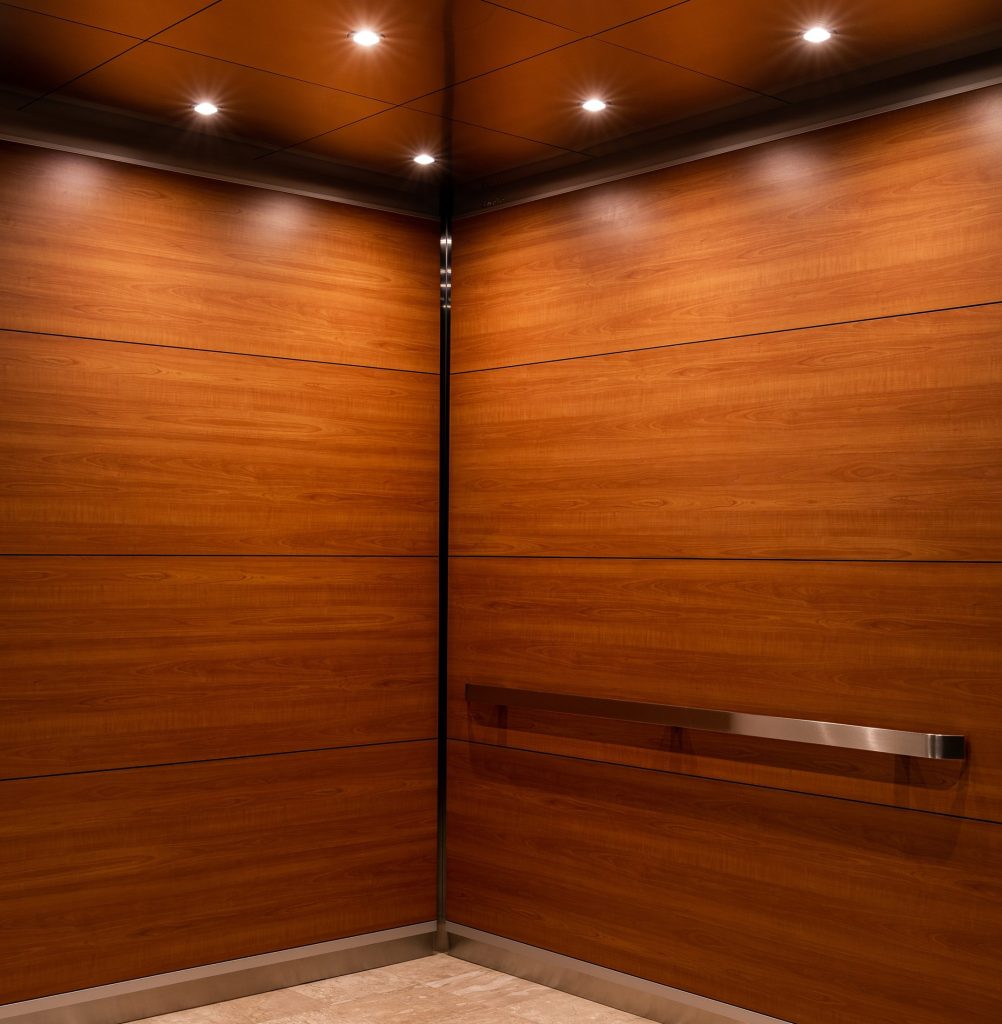 Elevator interior with wood-paneled walls, ceiling lights, and metal handrail