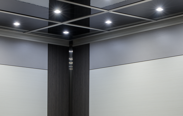 Modern elevator lighting design featuring an illuminated modular grid ceiling with recessed LED downlights inside a metallic gray cab interior.
