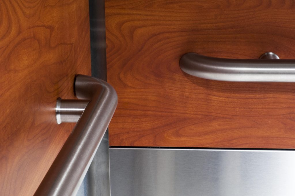 Close-up of a modern stainless steel handrail cleanly mounted to a textured gray and silver elevator wall panel.