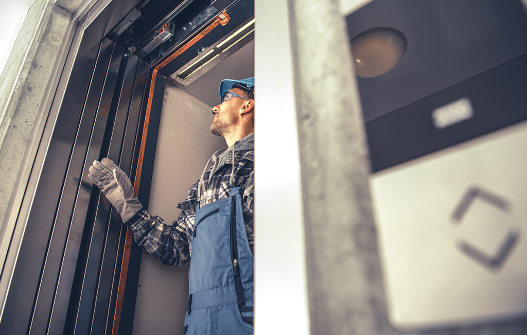 Elevator technician wearing a hard hat and safety gear inspecting an elevator cab door frame during an interior upgrade.
